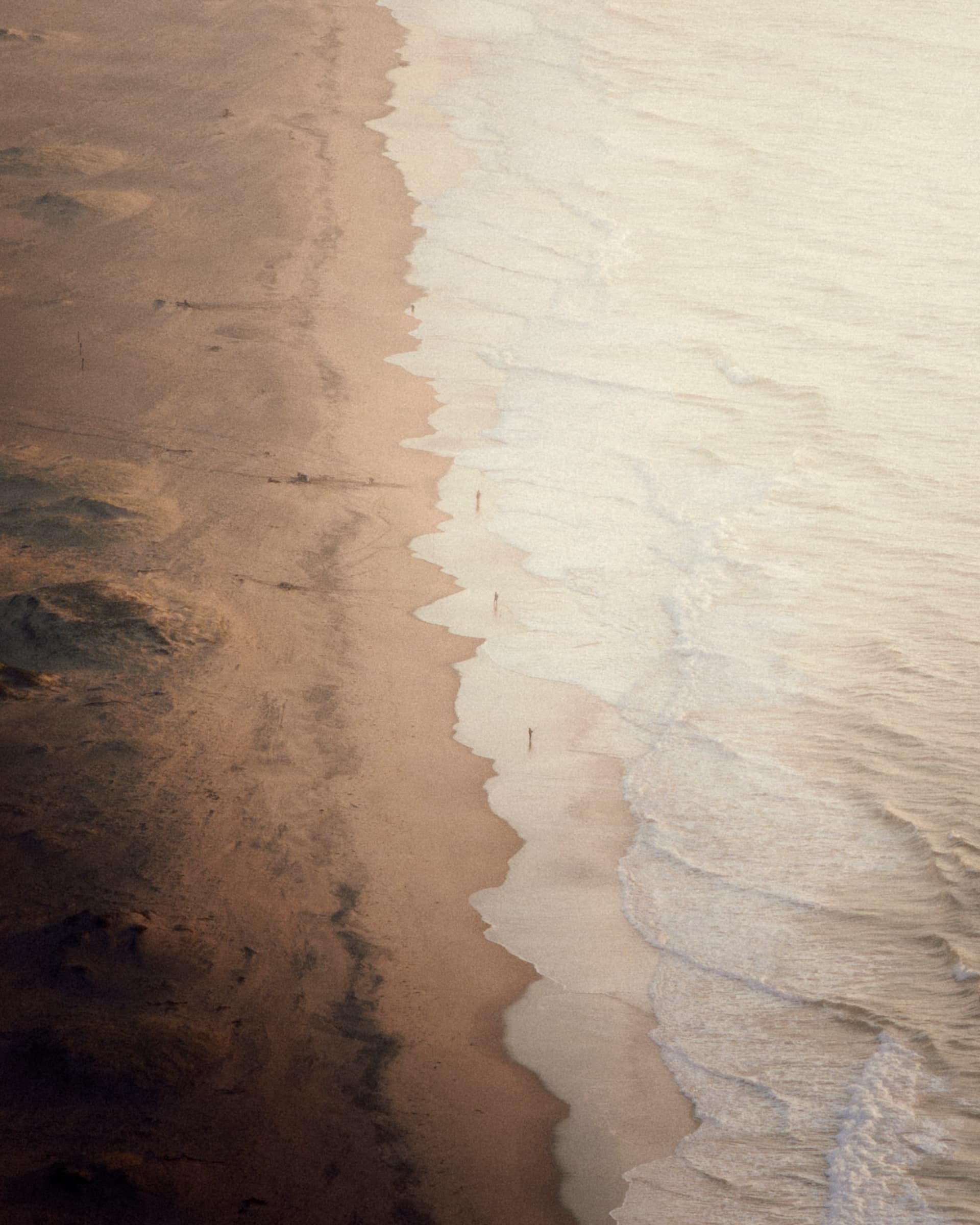 Drohnenaufnahme einer Strandlandschaft im Morgenlicht, die Brandung zeichnet Linien in den Sand