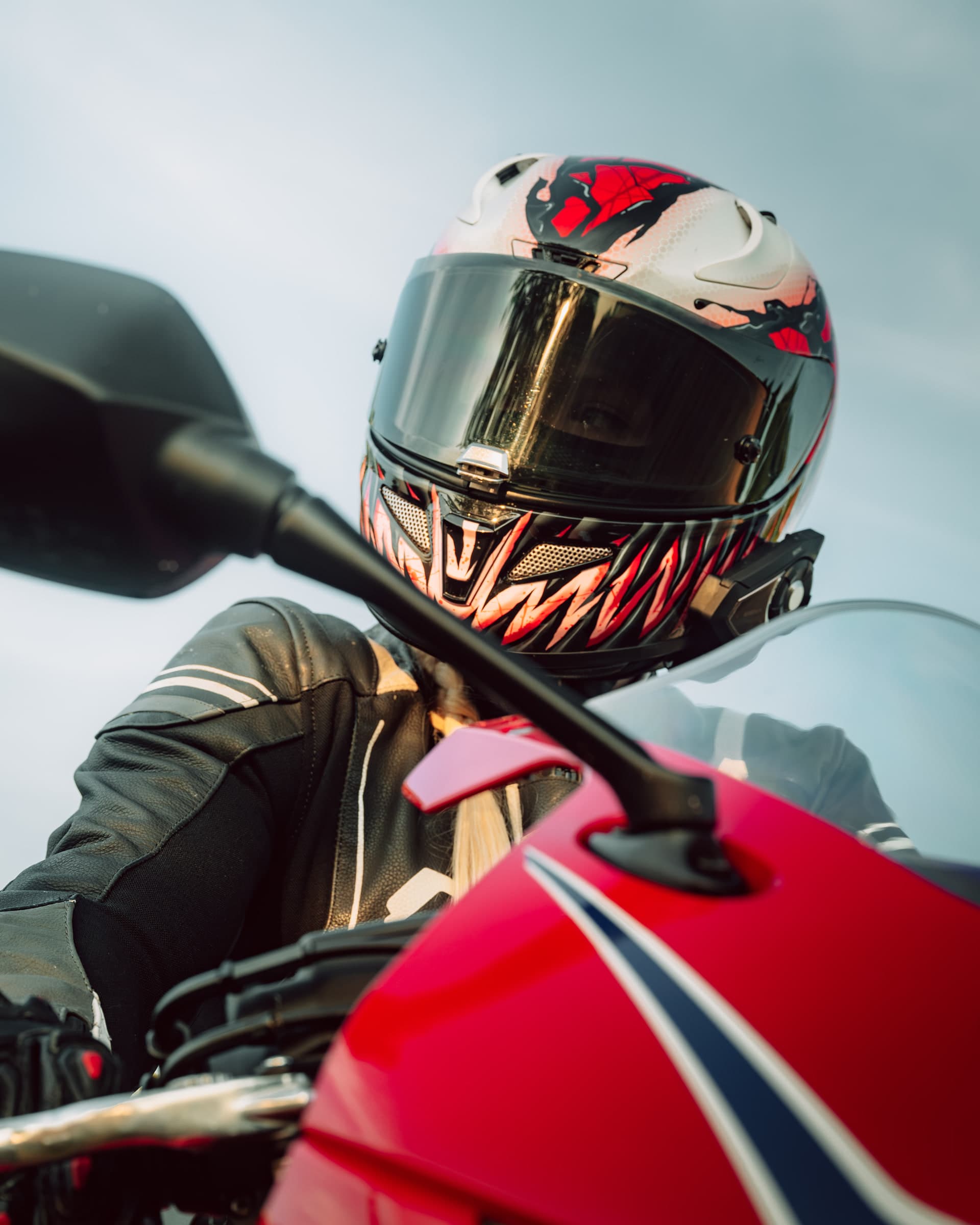 Nahaufnahme einer Motorradfahrerin auf roter Honda CBR mit rot-schwarzem Helmdesign