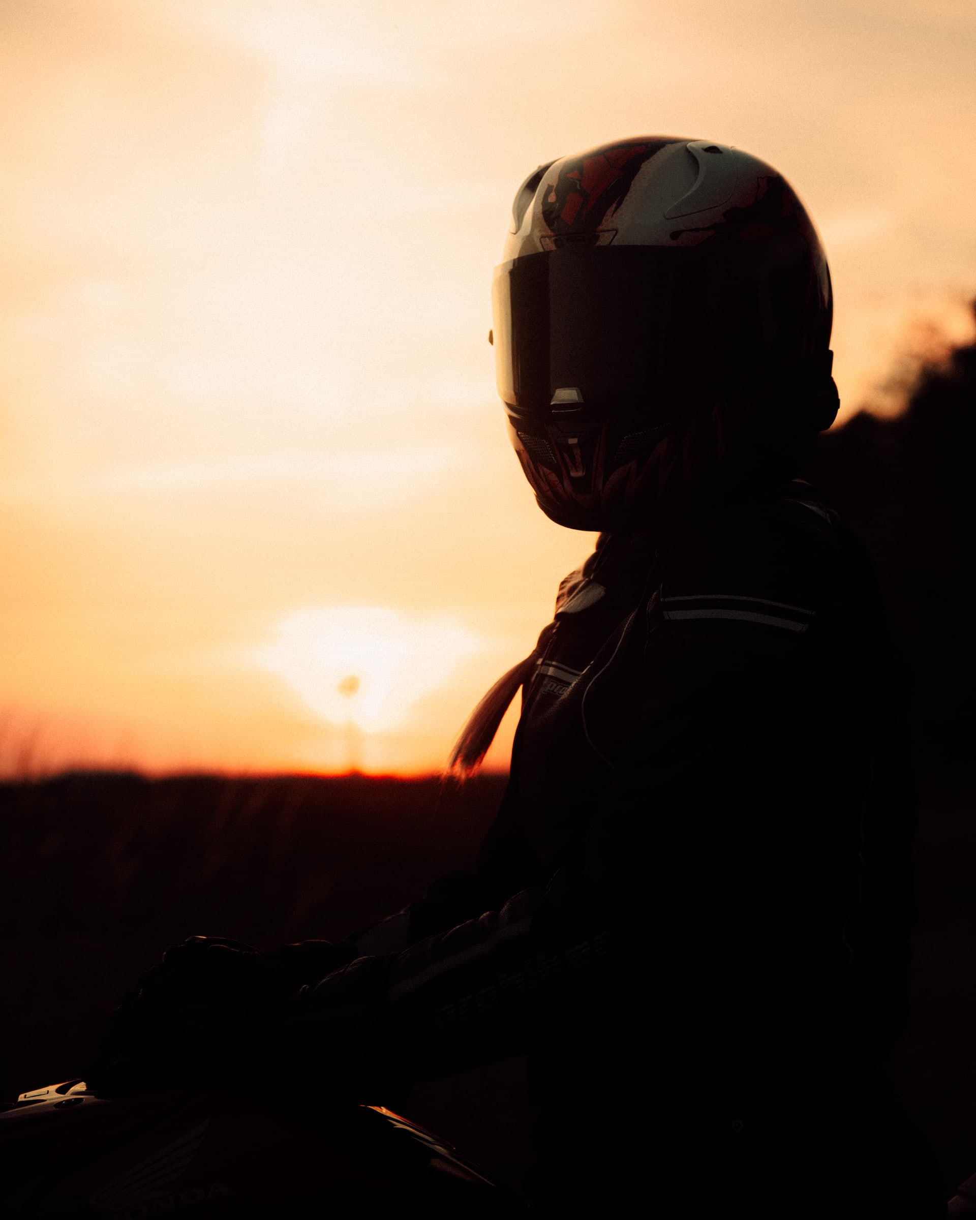 Motorradfahrerin in Silhouette auf einer Honda vor orangem Sonnenuntergang