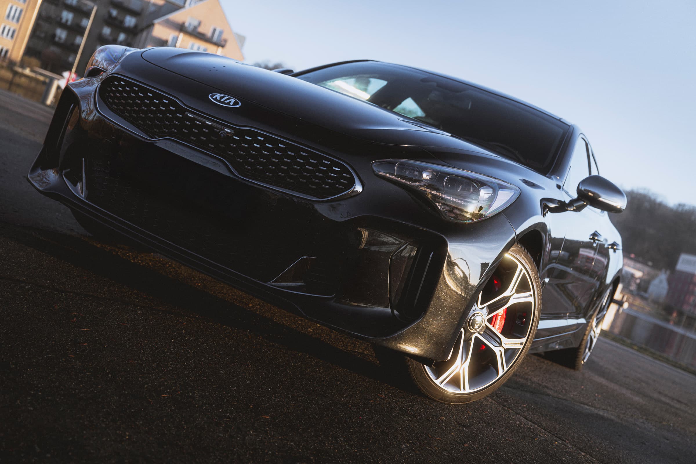 Kia Stinger in Frontansicht während der blauen Stunde, Scheinwerfer gegen den dunkelblauen Abendhimmel
